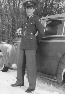 A photo of Mike Raddick, Sr. in front of a car wearing a U.S. Army uniform
