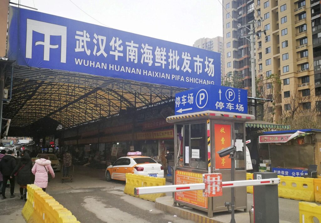 A blue sign saying 'Wuhan South China Seafood Market' in Chinese above a gate and parking sign